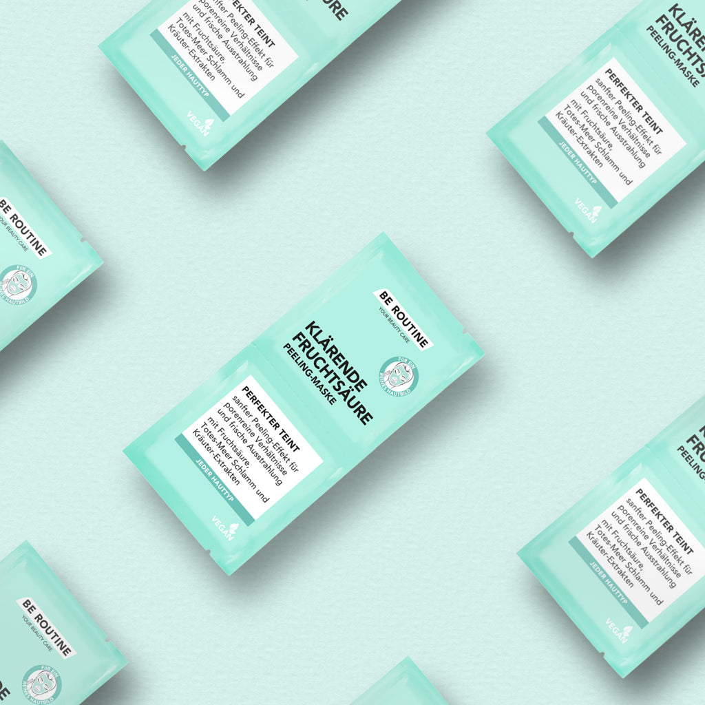 Abgebildet sind mehrere Verpackungen der Klärenden Fruchtsäure Peeling-Maske von be routine auf hellblauem Hintergrund.